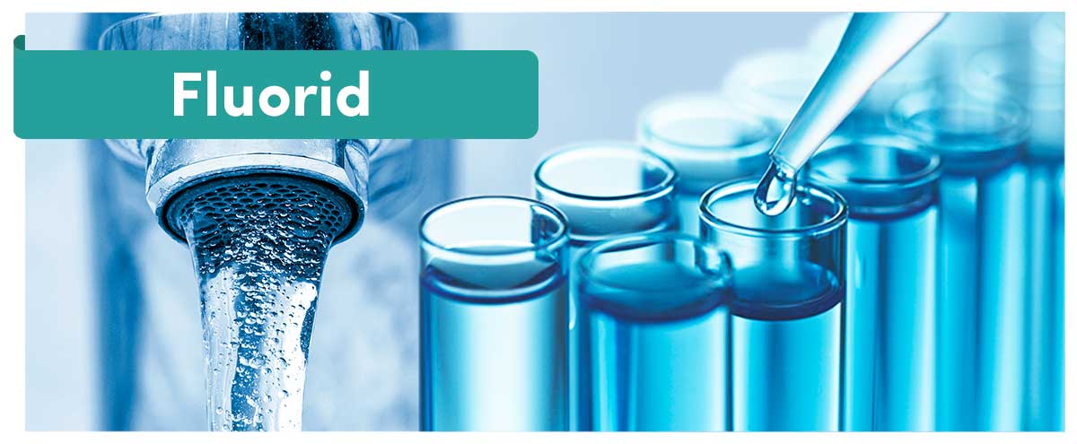 Fluorid-Schriftzug über laufendem Wasserhahn und einer Reihe blauer Reagenzgläser