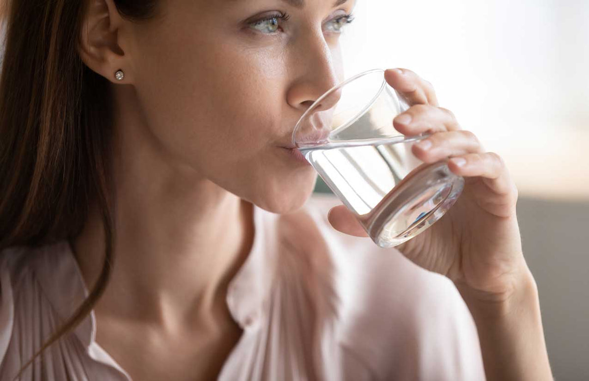 Frau in rosa Bluse trinkt in Seitenansicht aus einem Glas mit klarem Wasser