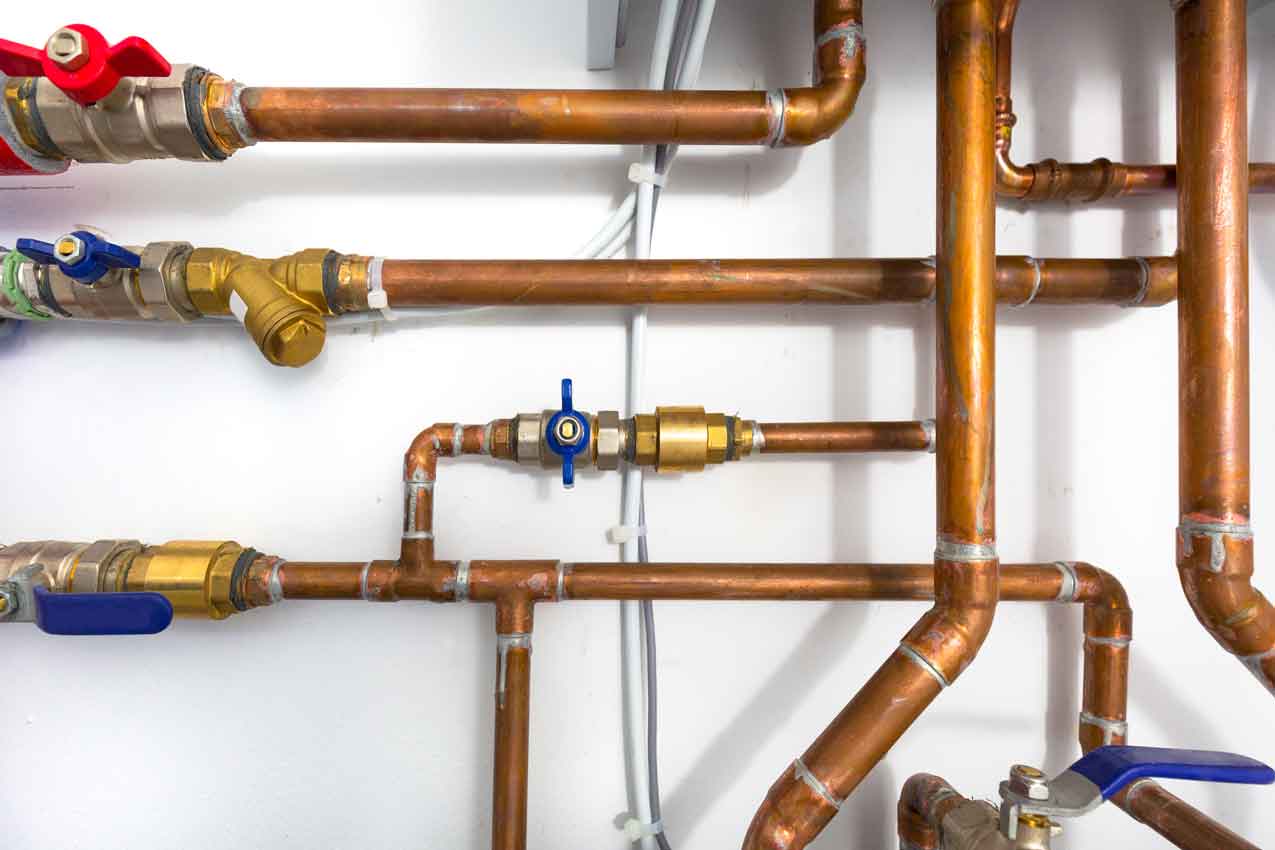 Verzweigte Kupferrohre mit Messingfittings und Absperrventilen an einer weißen Wand