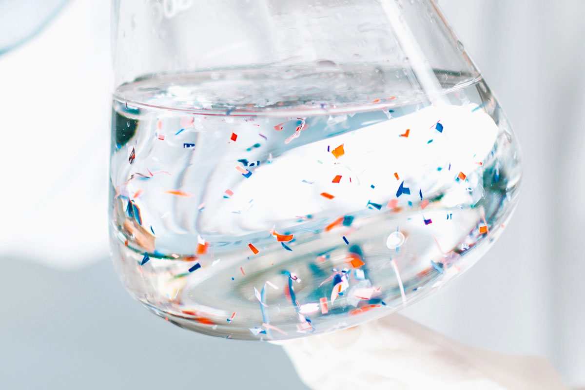 Erlenmeyerkolben mit Wasser und bunten Mikroplastikpartikeln in behandschuhter Hand