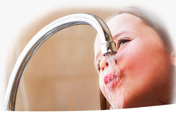 Kleines Mädchen trinkt direkt aus dem gebogenen Küchenhahn, Wasserstrahl läuft übers Gesicht