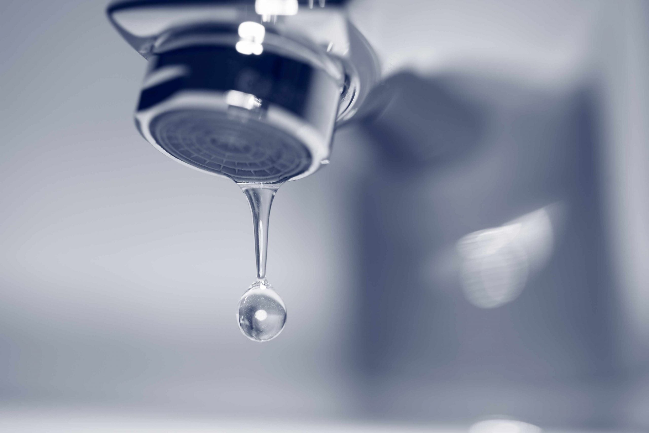 Einzelner Wassertropfen löst sich vom Perlator eines Wasserhahns, Nahaufnahme in Blaugrau