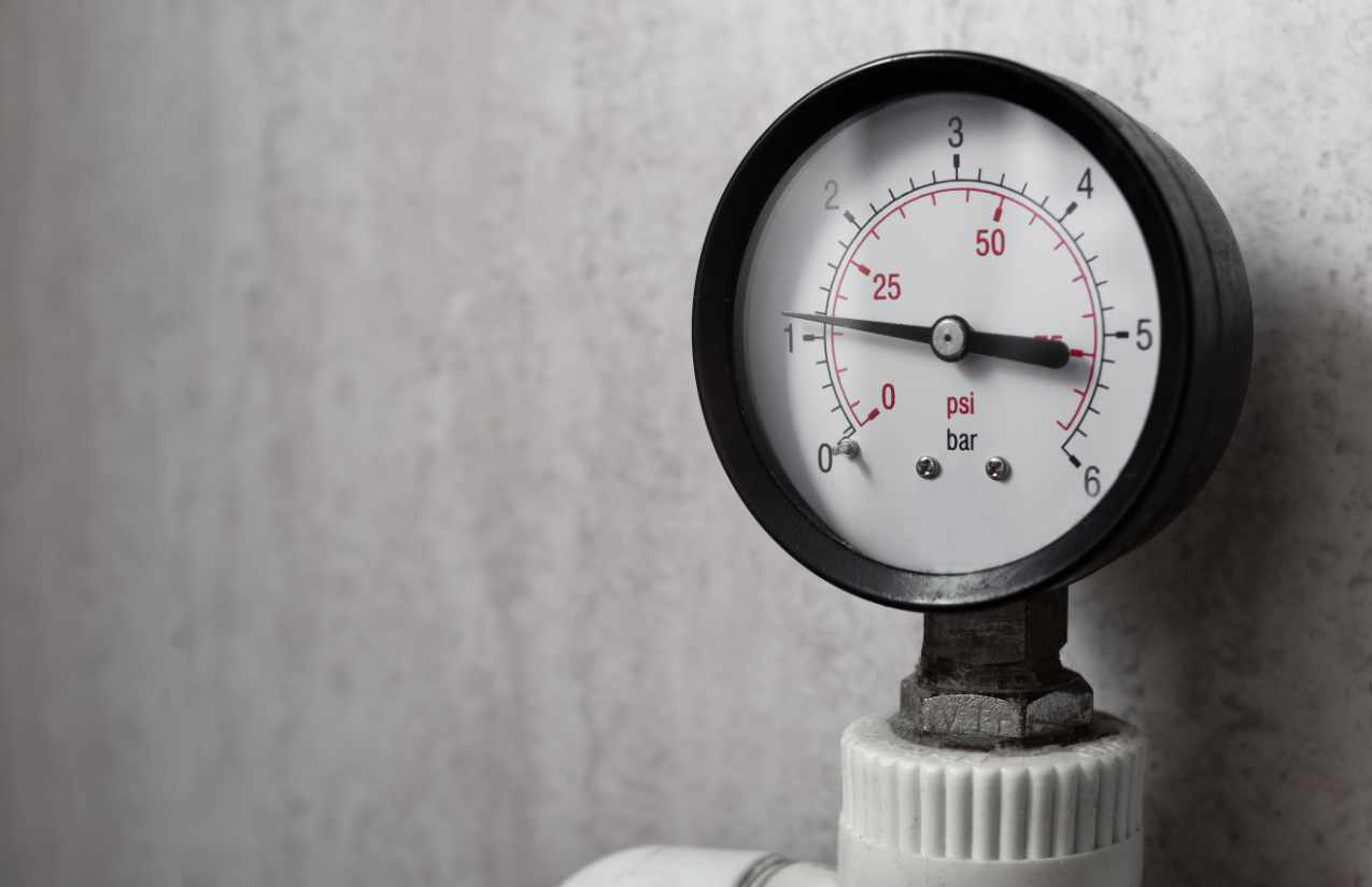 Manometer mit bar- und psi-Skala an einer Wasserleitung vor grauer Betonwand