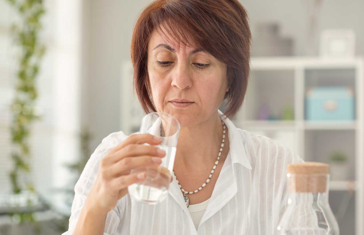 Frau betrachtet skeptisch ein Glas Wasser, daneben eine Glaskaraffe auf dem Tisch